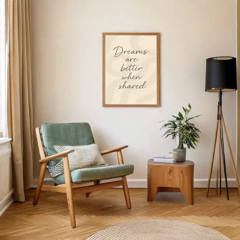 Framed 'Dreams are better when shared' quote print in an oak frame, styled in a warm Japandi living corner with a sage green armchair, wooden side table and tripod floor lamp.